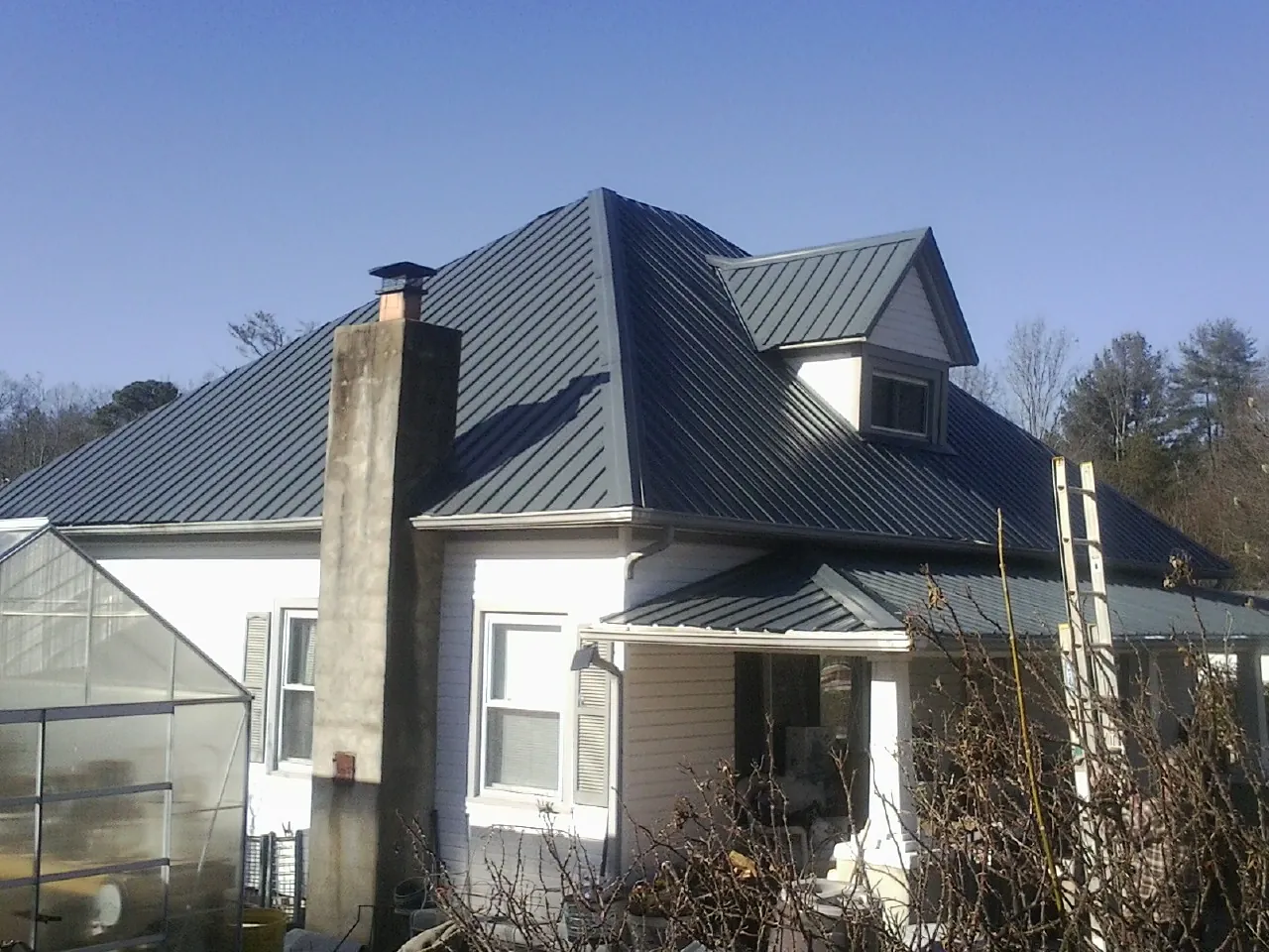 Dark blue standing seam metal roof on a white farmhouse with dormer — Slate & Tile Roof Repair by Roofing Brothers in Biggs