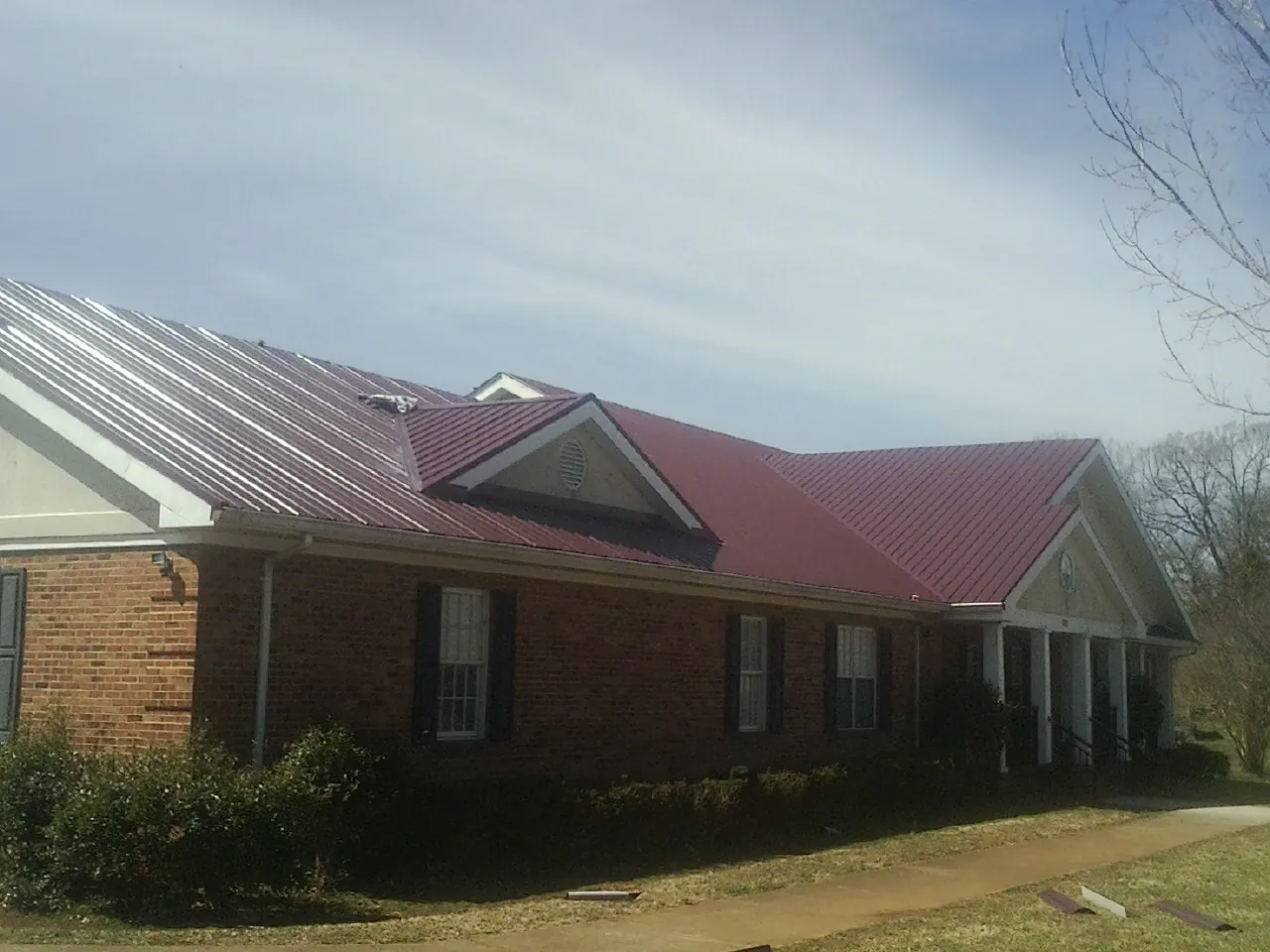 Red metal roof with gabled entries on a long brick building, from a Hail Damage Roof Repair job in Biggs