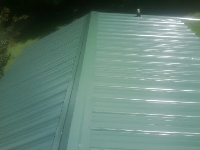 New green metal panels meeting at the ridge of a roof — Flat Roof Repair work by our crew in Biggs