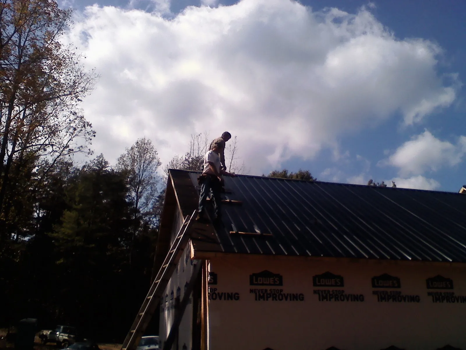 Roofer fastening dark metal panels high against a cloudy sky, from a Roof Inspection job in Biggs